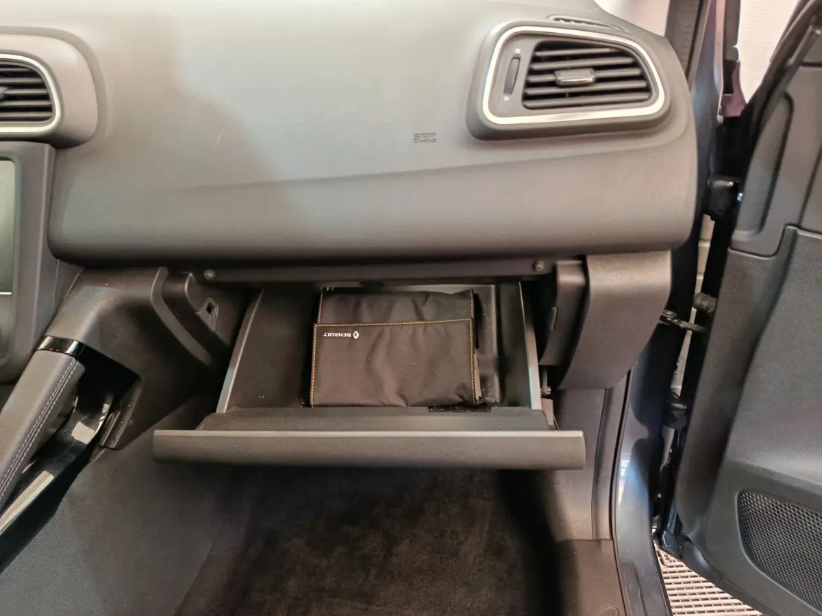 Gros plan sur la boîte à gants ouverte côté passager du Renault Kadjar gris foncé avec pochette Renault visible.