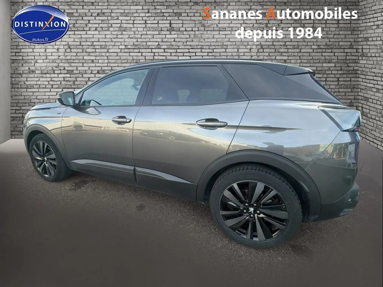 Vue latérale gauche d’un Peugeot 3008 gris foncé avec jantes noires et toit noir brillant, sur fond de mur en briques.