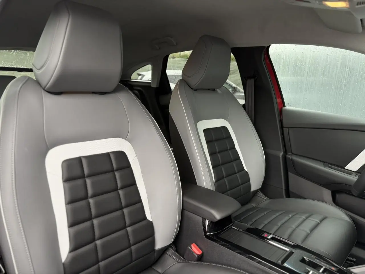 Vue intérieure des sièges avant gris clair et noir de la Citroën C4 Hybrid 2025 avec accoudoir central et porte-gobelets.