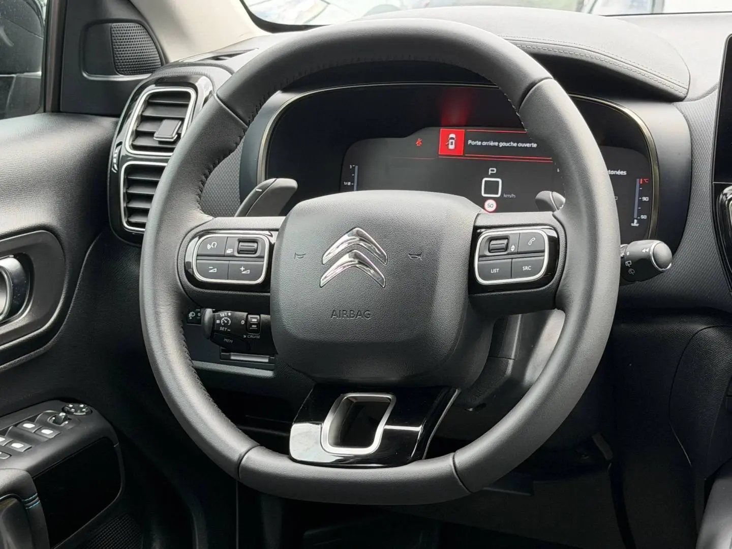 Vue rapprochée du volant cuir multifonction noir du Citroën C5 Aircross 2025 avec tableau de bord numérique allumé.
