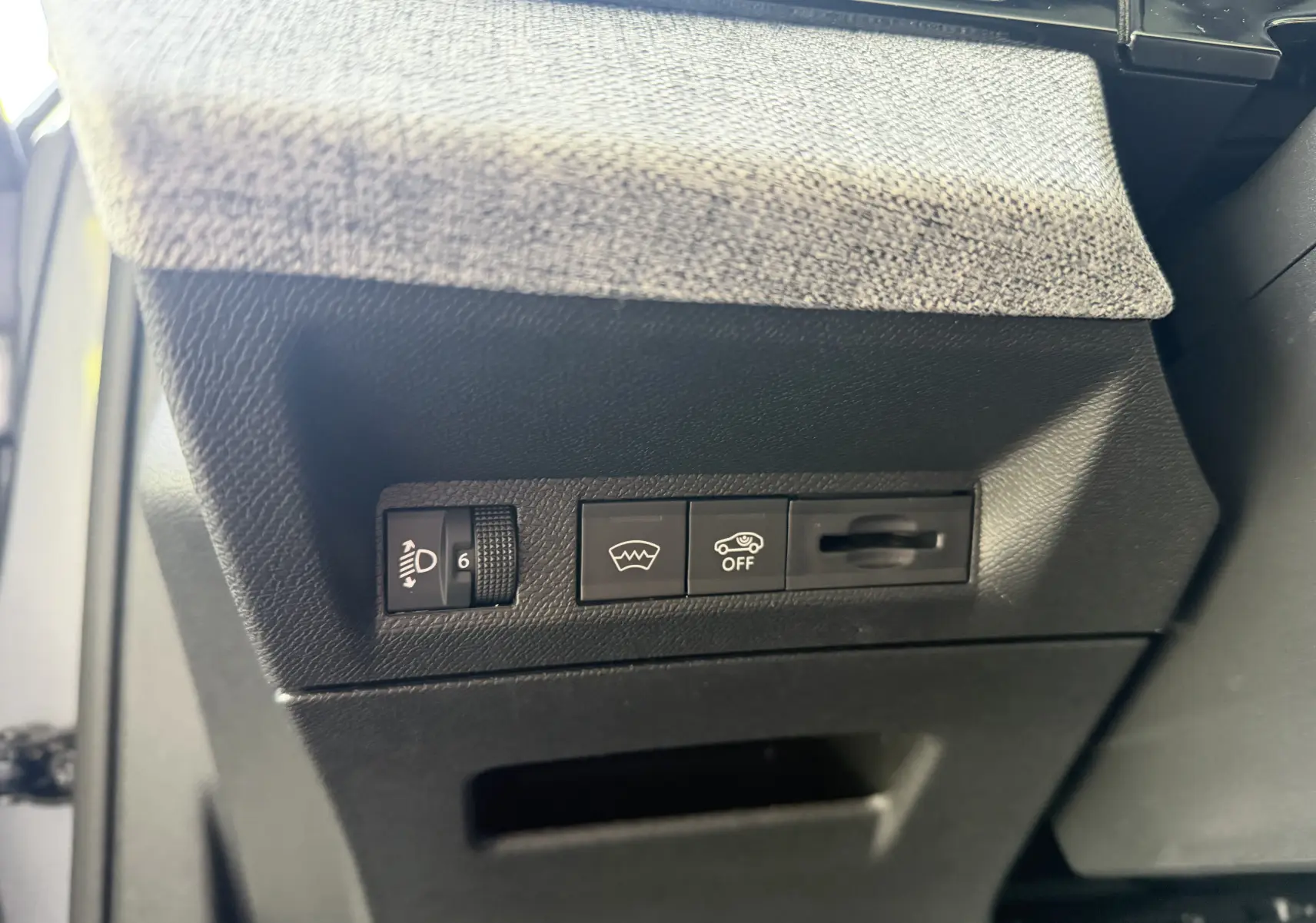 Détail intérieur côté gauche du tableau de bord gris artense de la Peugeot 1007 Hybrid avec commandes de réglage des phares et aides à la conduite.