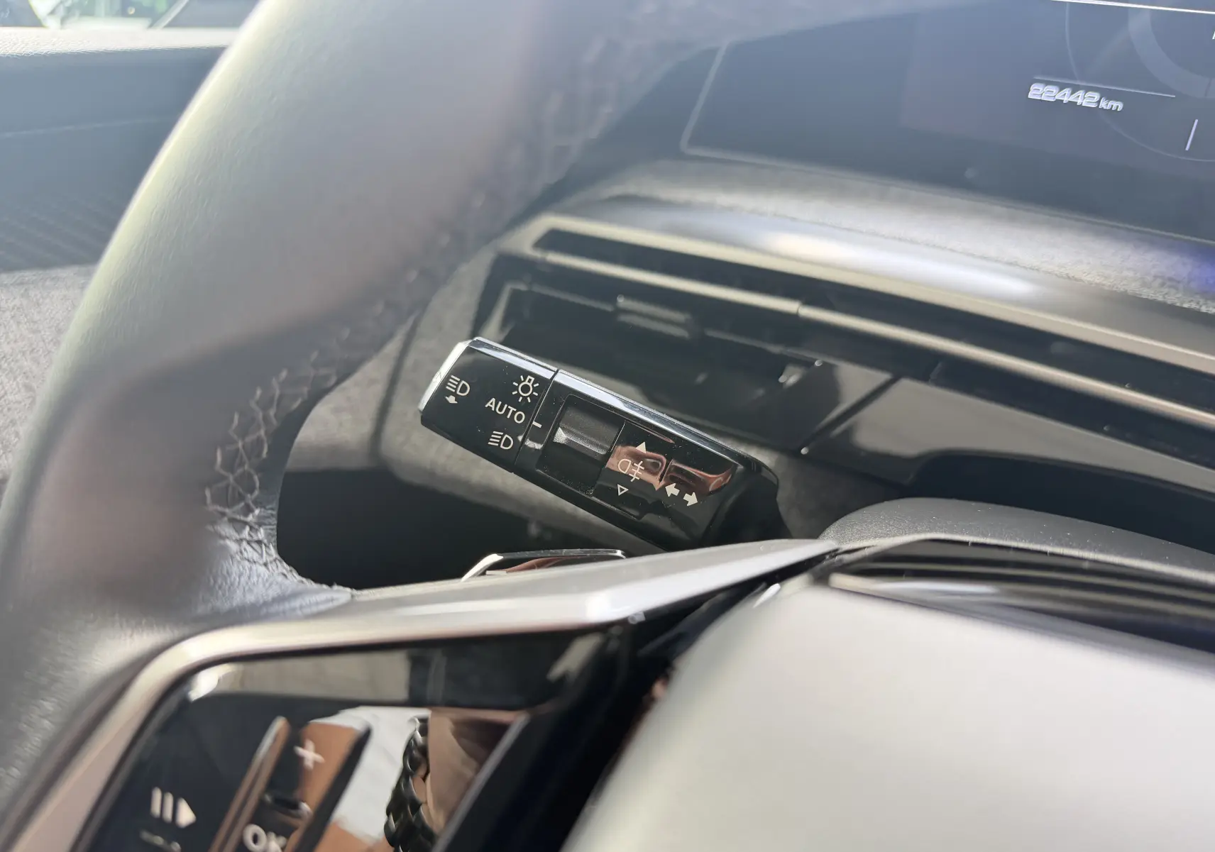 Gros plan sur la commande des feux au volant d’un Peugeot 1007 gris artense, intérieur moderne et épuré.
