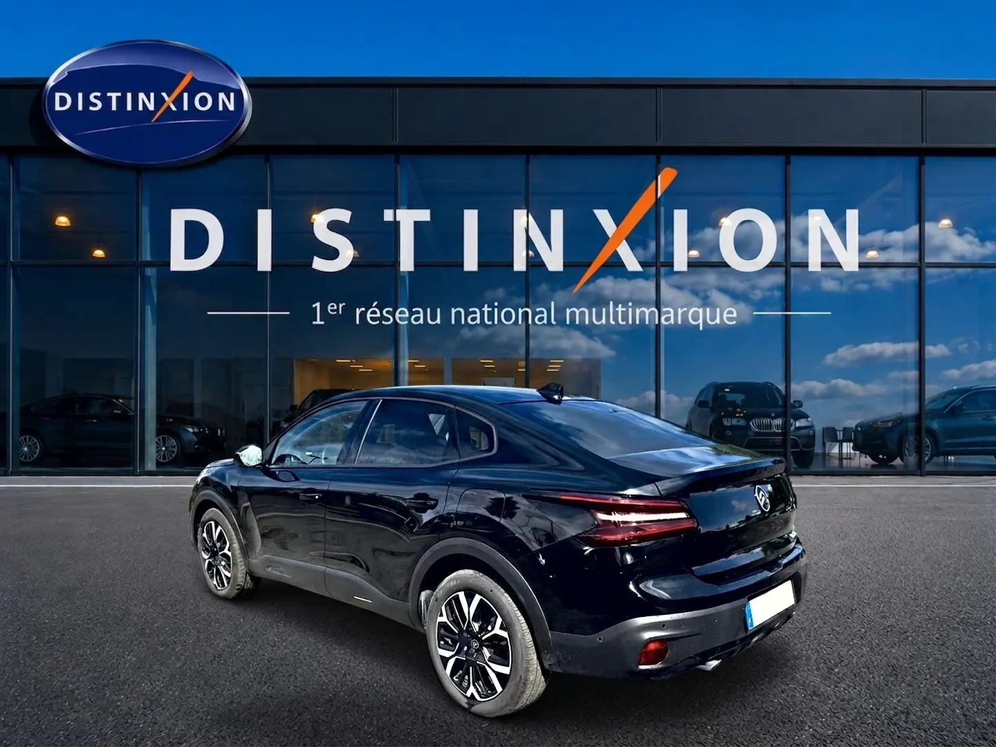 Vue 3/4 arrière droite d'une Citroën C4 X noire 2025 avec feux arrière LED et jantes alu devant un showroom Distinxion.