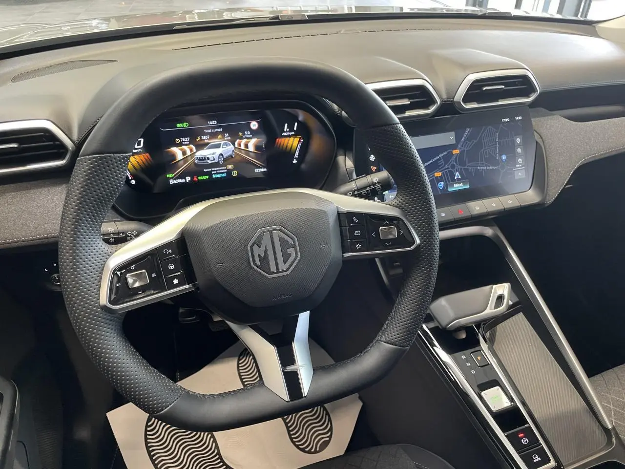 Vue intérieure centrée sur le volant cuir et le tableau de bord numérique du MG ZS 1.5 Hybrid+ gris clair, avec écran tactile.