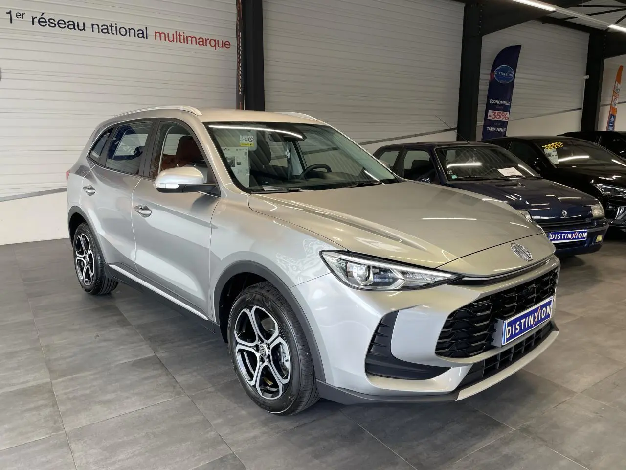 MG ZS 1.5 Hybrid+ gris clair en 3/4 avant droit, avec jantes alliage et calandre noire distinctive.