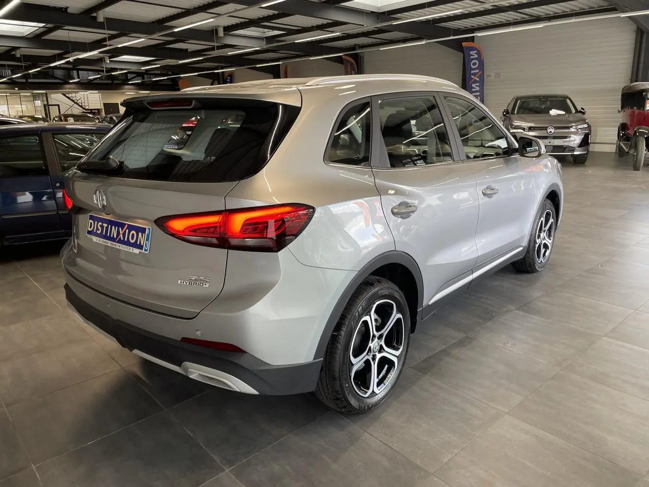 Vue 3/4 arrière droite du MG ZS 1.5 Hybrid+ gris clair avec feux LED allumés en showroom.