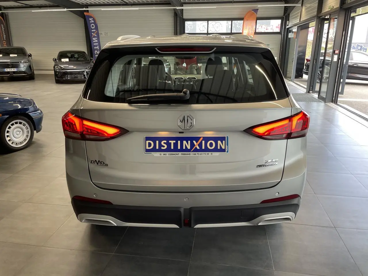 Vue arrière d’un MG ZS 1.5 Hybrid+ gris clair avec feux arrière LED allumés en showroom.