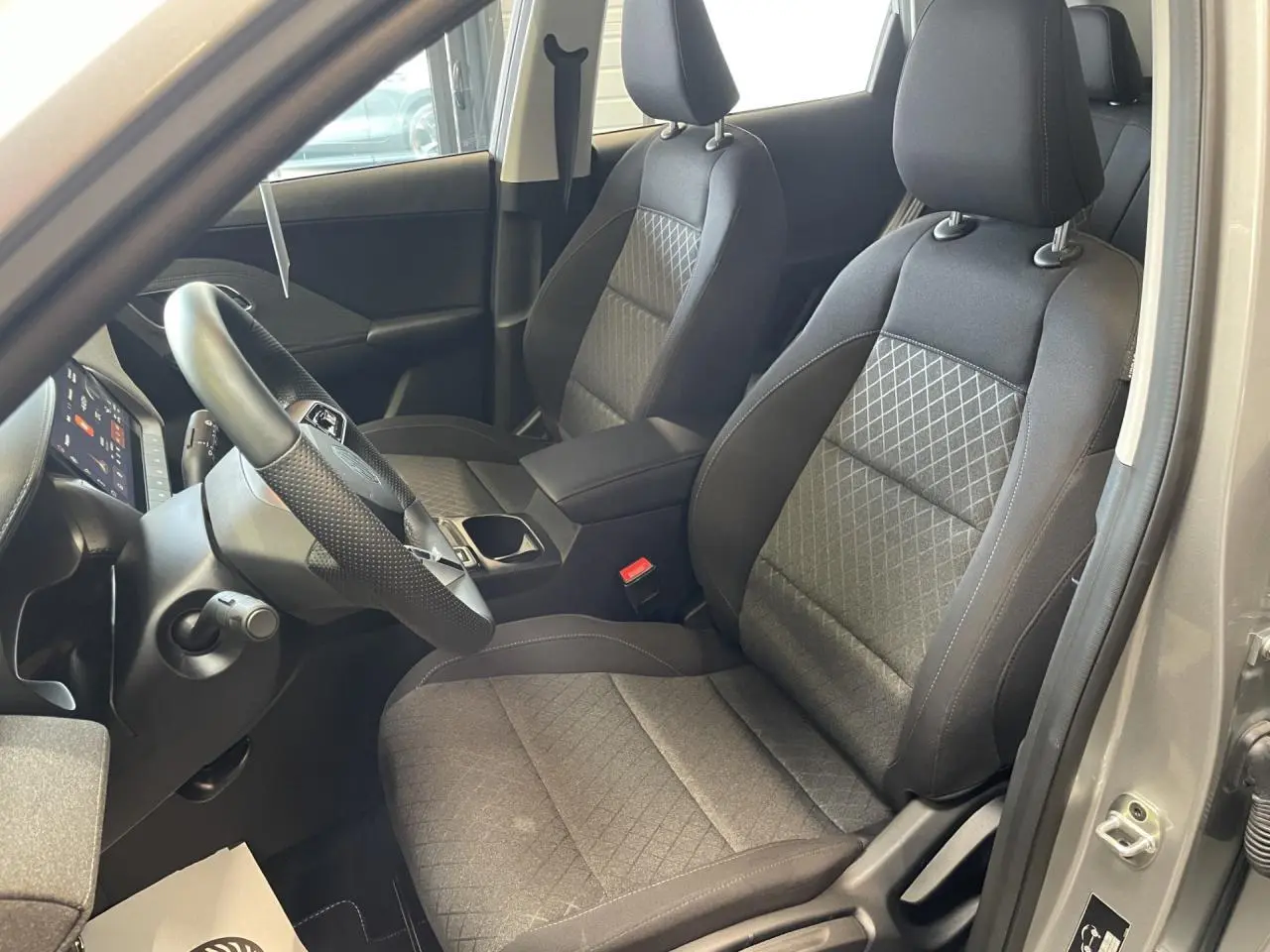 Vue intérieure côté conducteur du MG ZS 1.5 Hybrid+ 2026, sièges tissu noir avec motifs losanges et volant cuir.