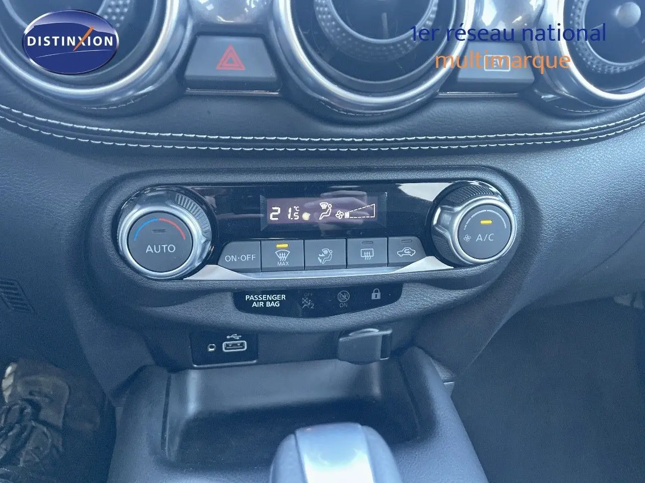 Gros plan sur la console centrale du Nissan Juke gris, montrant les commandes de climatisation automatique et la prise USB.