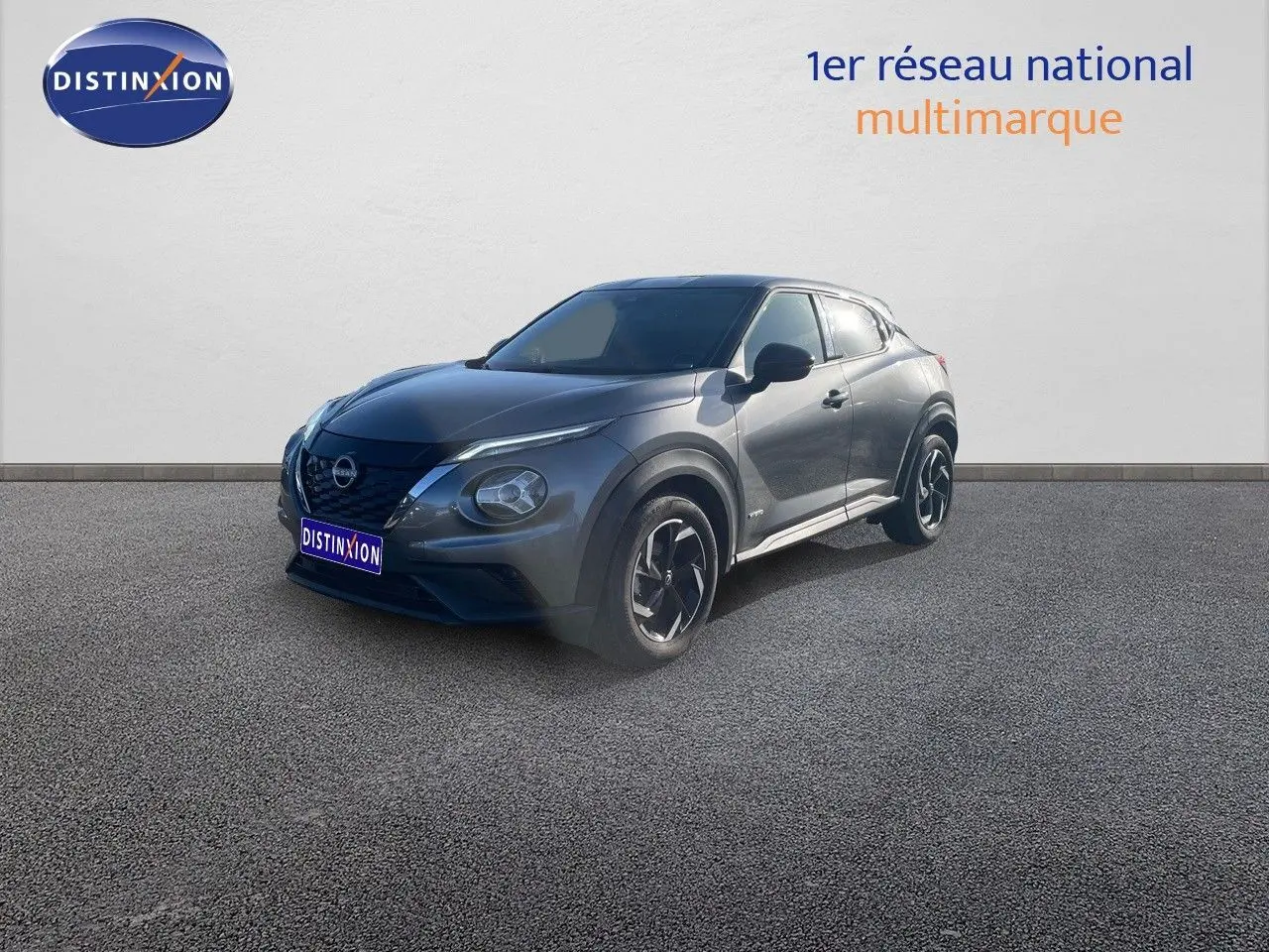 Nissan Juke 2024 gris squale métal en 3/4 avant droit, avec jantes biton et calandre noire distinctive.