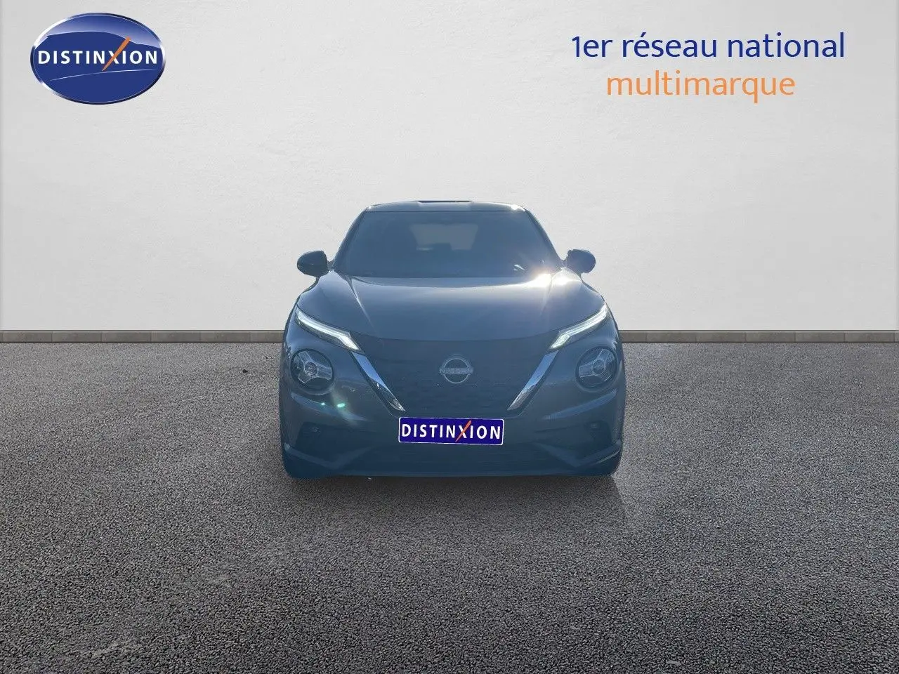 Vue frontale du Nissan Juke 1.6 HEV 143ch gris squale métal avec phares LED allumés sur fond neutre.