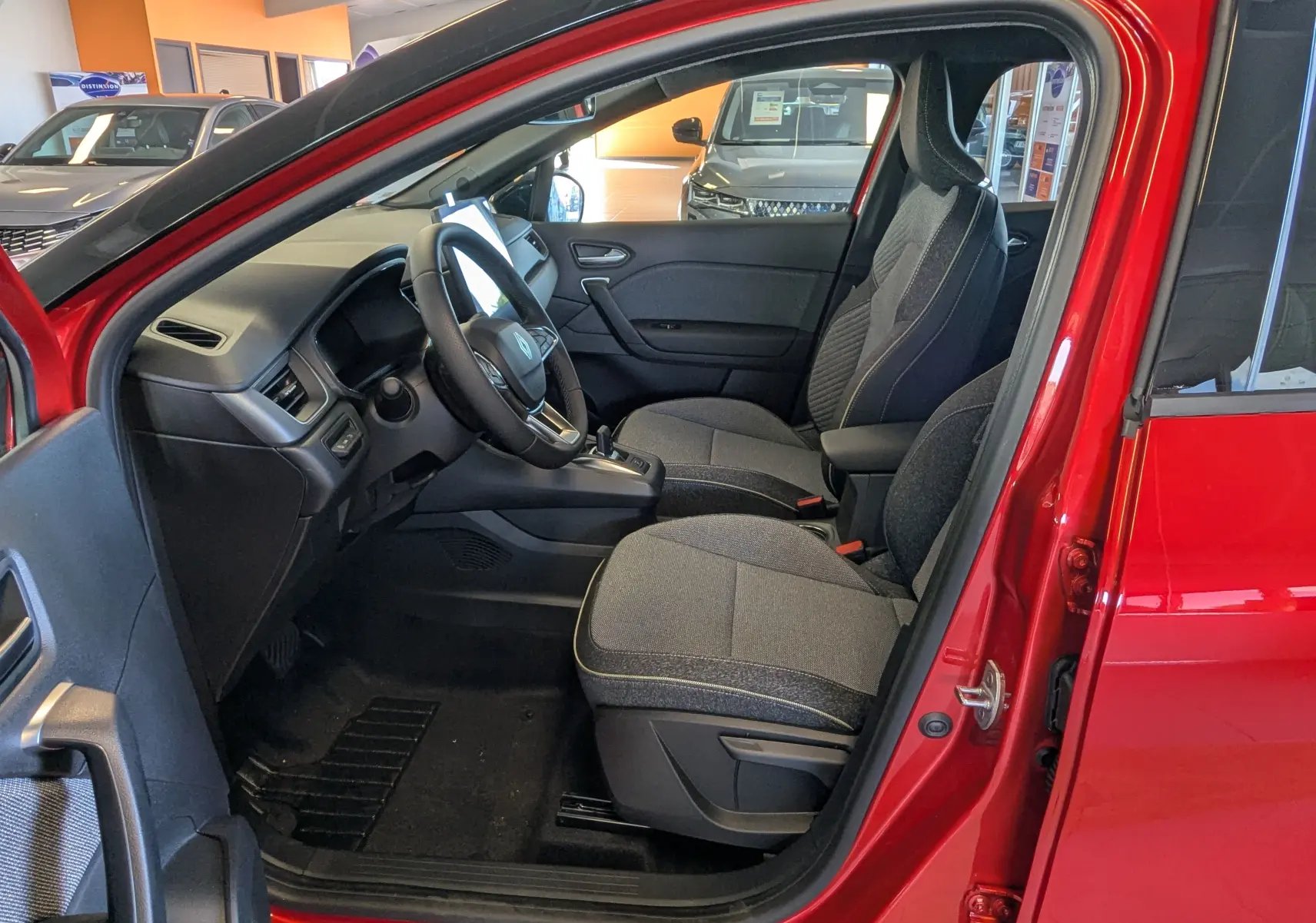 Intérieur côté conducteur du Renault Captur rouge flamme avec sièges tissu gris et tableau de bord moderne visible.