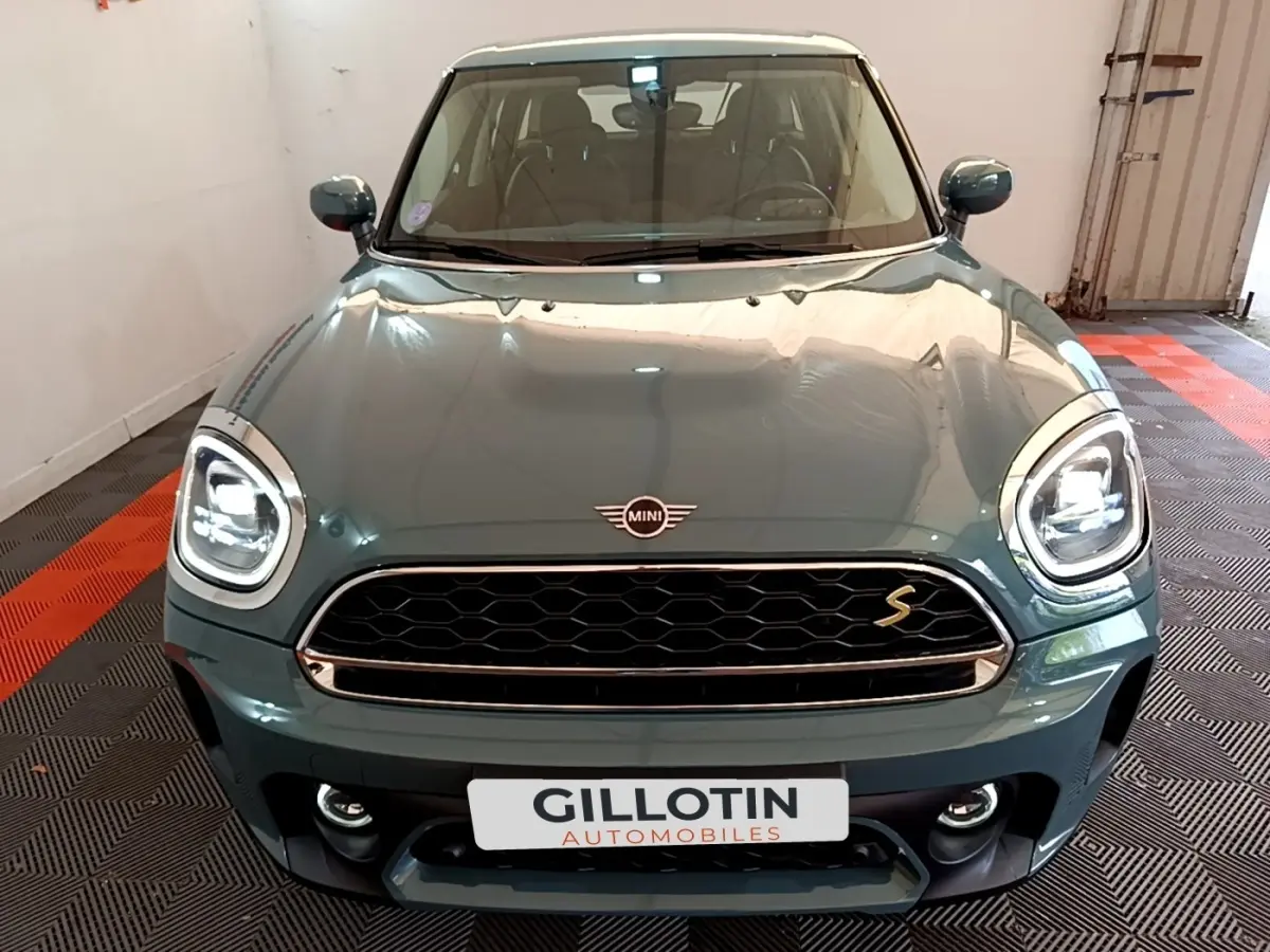 Vue avant d'une MINI Countryman Cooper SE hybride rechargeable vert avec phares LED et calandre noire en intérieur showroom.