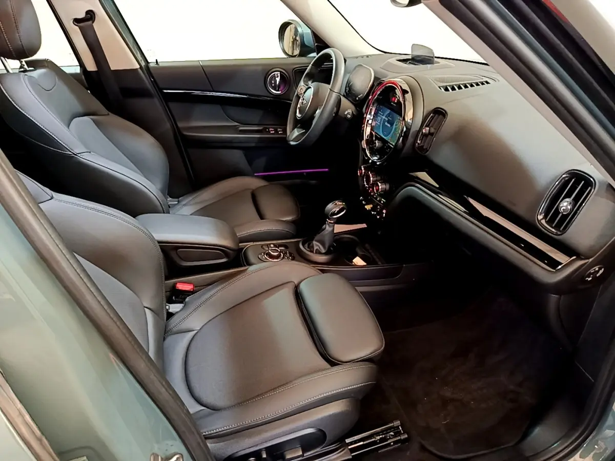 Intérieur avant droit du MINI Countryman vert 2023, sièges cuir noirs et tableau de bord avec écran tactile rond lumineux.