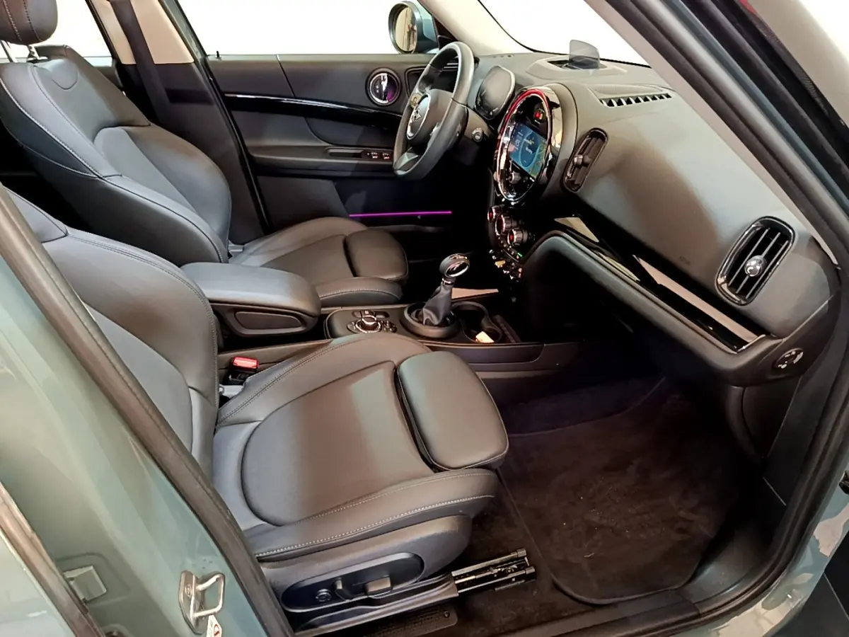 Intérieur avant droit du MINI Countryman vert 2023, sièges cuir noirs et tableau de bord avec écran tactile rond lumineux.