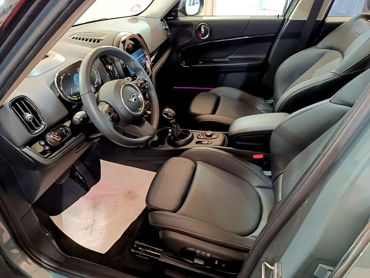 Intérieur avant droit du MINI Countryman vert 2023, sièges cuir noirs et tableau de bord avec écran tactile lumineux.