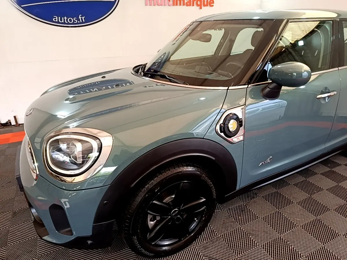 Vue 3/4 avant droit d'une MINI Countryman Cooper SE hybride rechargeable vert avec jantes noires et prise de charge latérale visible.