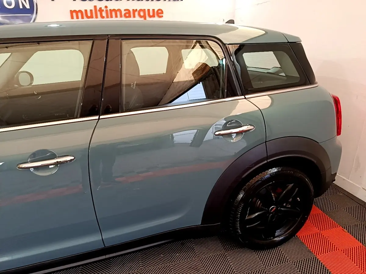 Vue côté droit arrière d'une MINI Countryman hybride rechargeable verte avec jantes noires brillantes et poignées chromées.
