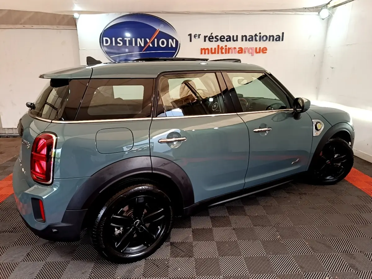Vue 3/4 arrière droite d'une MINI Countryman hybride rechargeable verte avec jantes noires et toit noir.