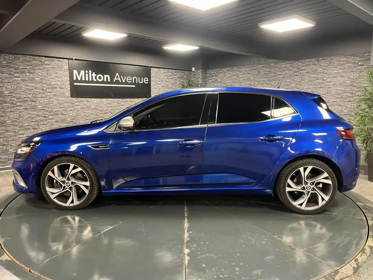 Profil droit d’une Renault Mégane GT bleu Iron 2016 avec jantes alliage 18 pouces et vitres surteintées.