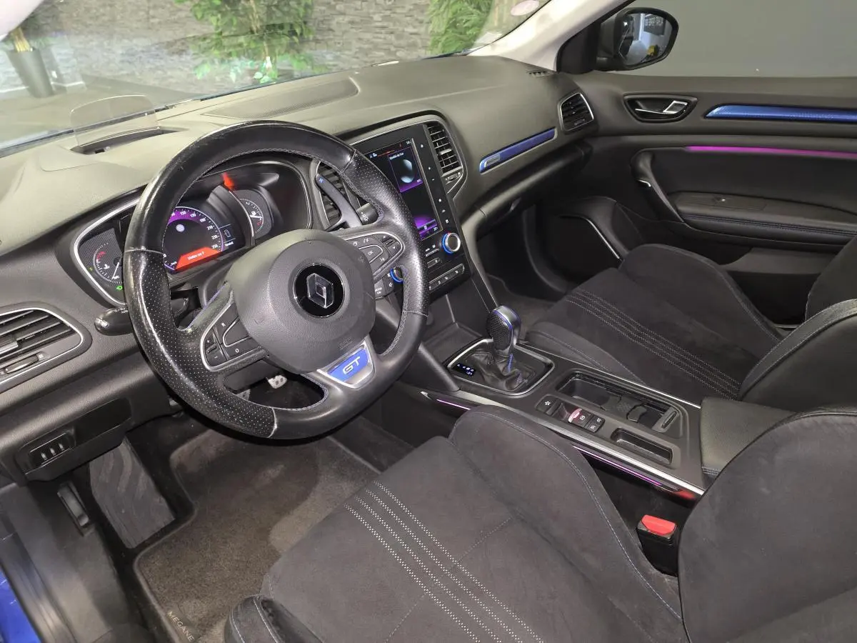 Vue intérieure côté conducteur de la Renault Mégane GT 2016 avec sellerie noire, volant GT et éclairage d’ambiance violet.
