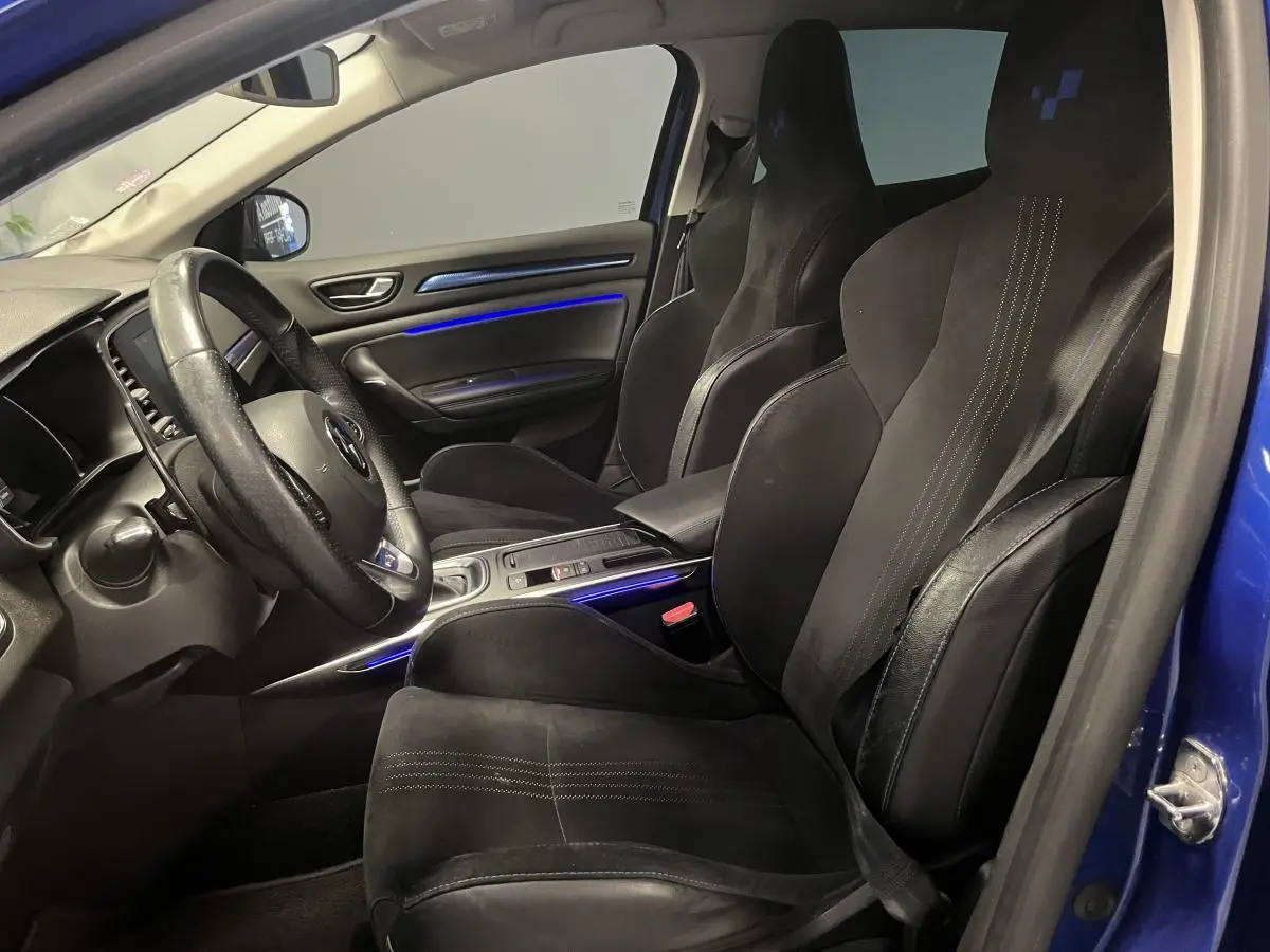 Vue intérieure côté conducteur de la Renault Mégane GT 2016 avec sièges sport noirs et éclairage d’ambiance bleu.