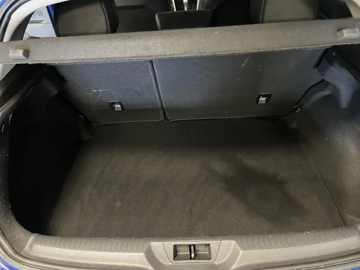 Vue plongeante sur le coffre vide de la Renault Mégane GT bleu, montrant la banquette arrière rabattable et le tapis noir.
