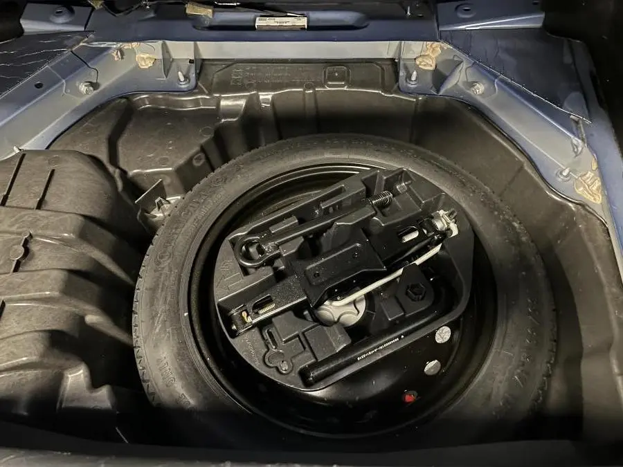 Vue plongeante sur la roue de secours galette noire dans le coffre bleu de la Renault Mégane GT 2016.