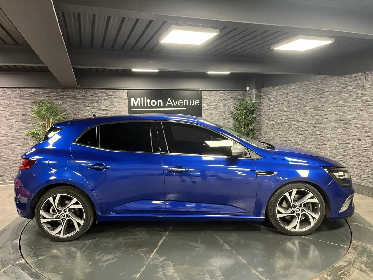 Profil droit d’une Renault Mégane GT bleu Iron 2016 avec jantes alliage 18 pouces et vitres surteintées.