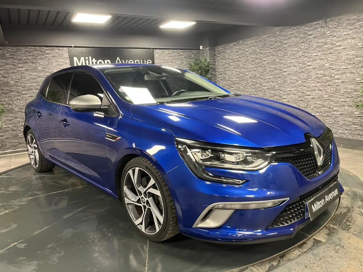 Renault Mégane GT bleu Iron en 3/4 avant droit, avec jantes alliage 18 pouces et calandre noire nid d'abeilles.