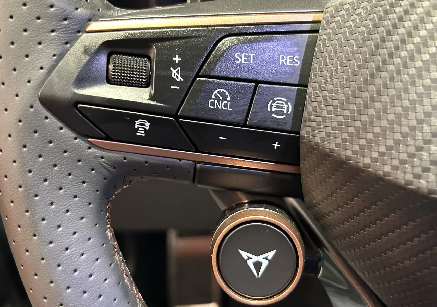 Gros plan sur les commandes noires du volant perforé avec logo CUPRA sur fond carbone.