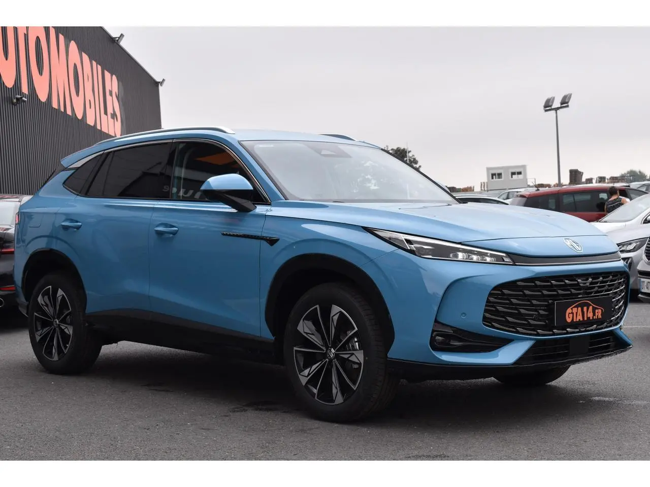 MG Motor EHS 1.5 Hybrid+ bleu 2026 en 3/4 avant droit, avec calandre large et jantes noires distinctives.