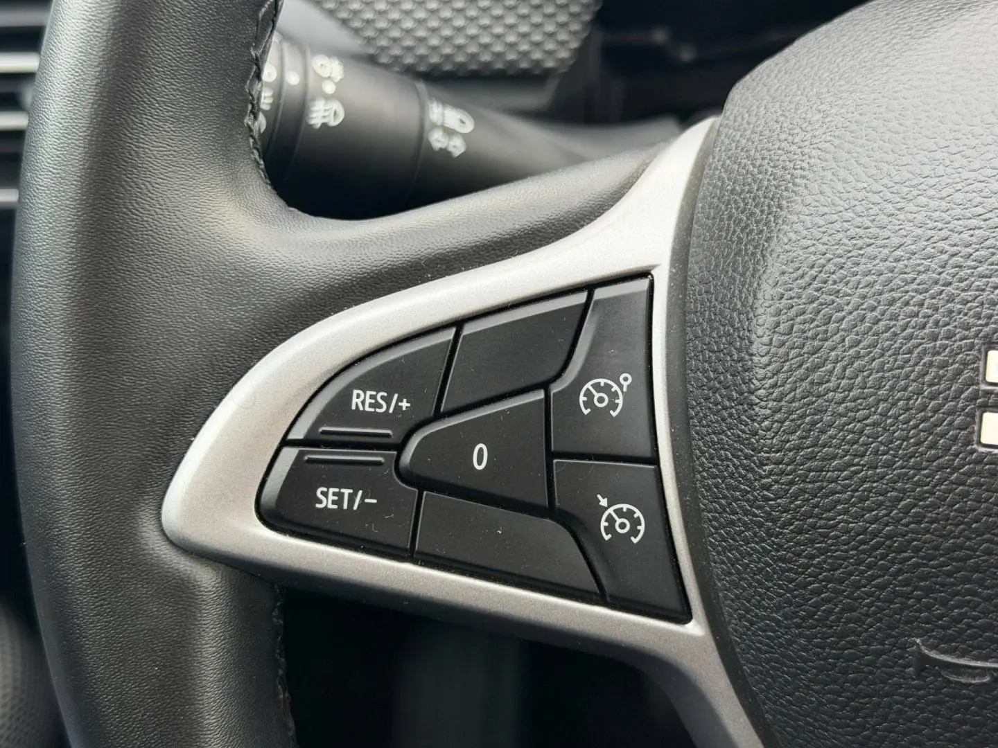 Gros plan sur les commandes du régulateur de vitesse au volant noir du Dacia Jogger Vert Cèdre métallisé.