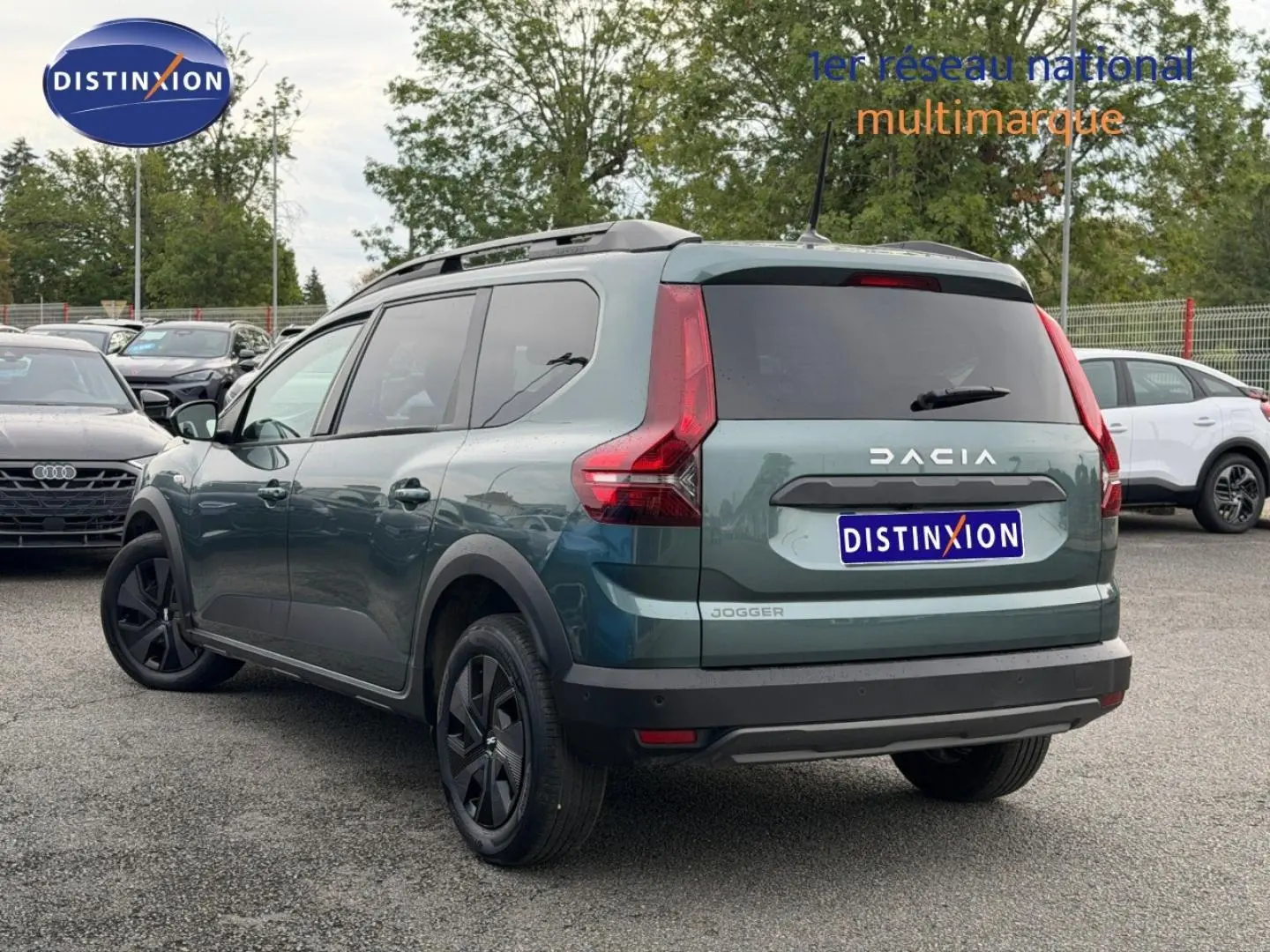 Vue 3/4 arrière droite d'un Dacia Jogger 2025 vert cèdre métallisé avec barres de toit et vitres arrière surteintées.