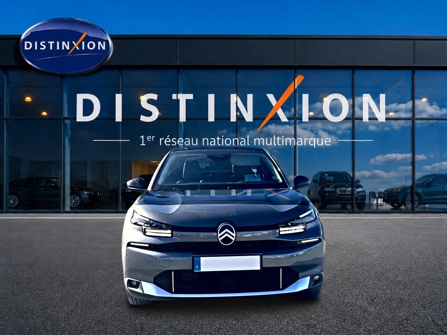 Vue frontale d'une Citroën C4 X gris mercure devant une vitrine avec logo Distinxion en arrière-plan.