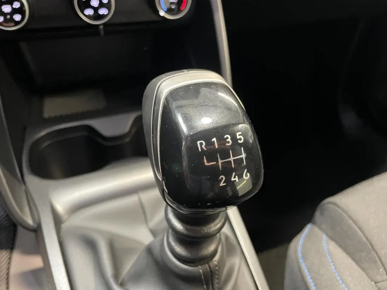 Gros plan sur le levier de vitesses manuel noir dans l’habitacle sombre de la Citroën C3 blanche.