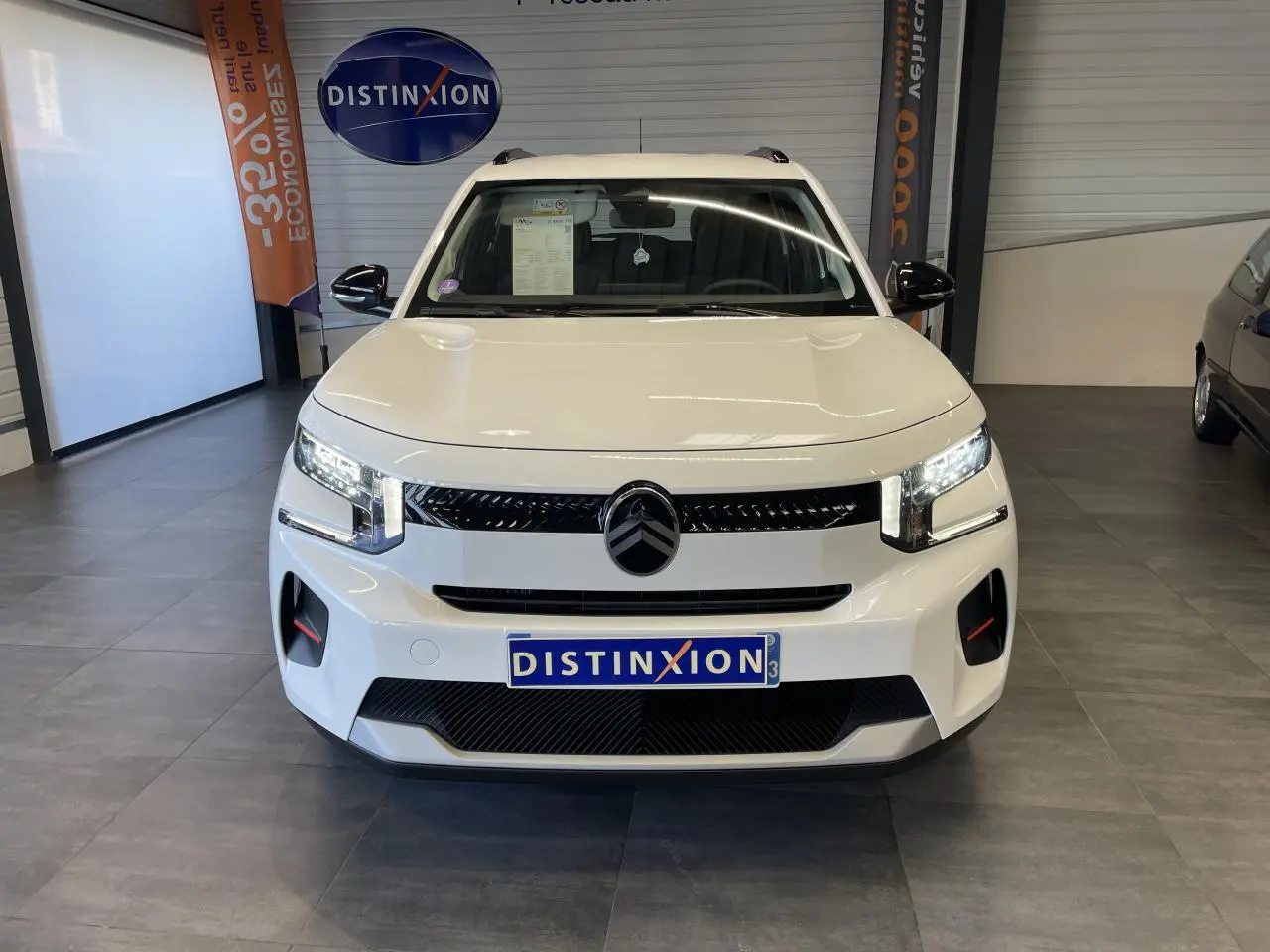 Vue frontale d'une Citroën C3 blanche avec calandre noire brillante et projecteurs LED allumés en showroom.