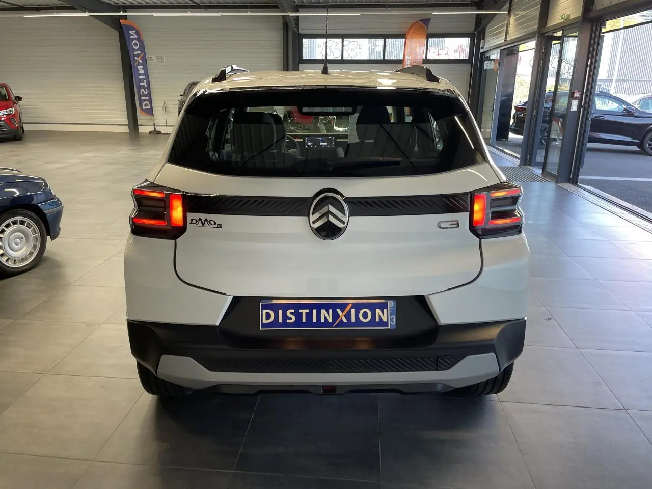 Vue arrière d'une Citroën C3 blanche 2025 avec feux LED et barres de toit noir brillant en showroom.