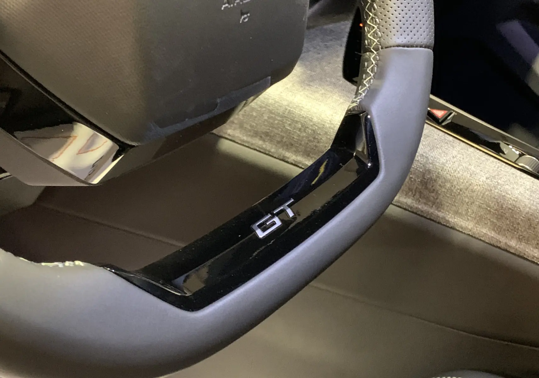 Gros plan sur le volant GT en cuir perforé du Peugeot 3008 III Hybrid 136, intérieur gris avec surpiqûres contrastées.