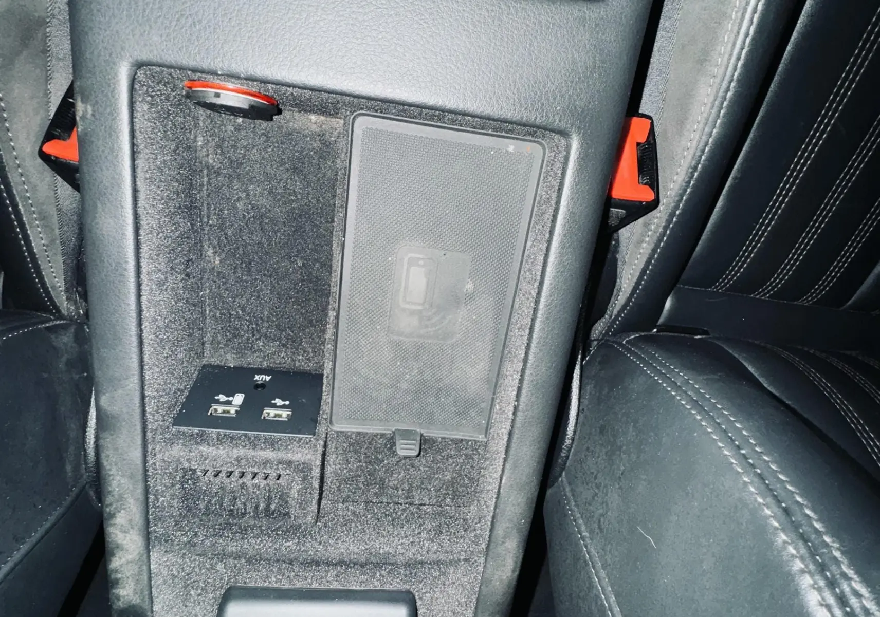 Vue rapprochée de la console arrière noire de l'Audi A6 Avant Allroad, avec ports USB et prise 12V visibles entre les sièges cuir noir.