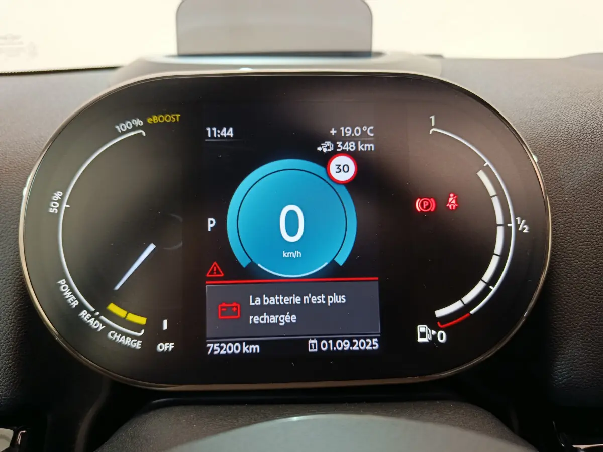 Tableau de bord numérique du MINI Countryman hybride, affichant vitesse zéro et alerte batterie déchargée.