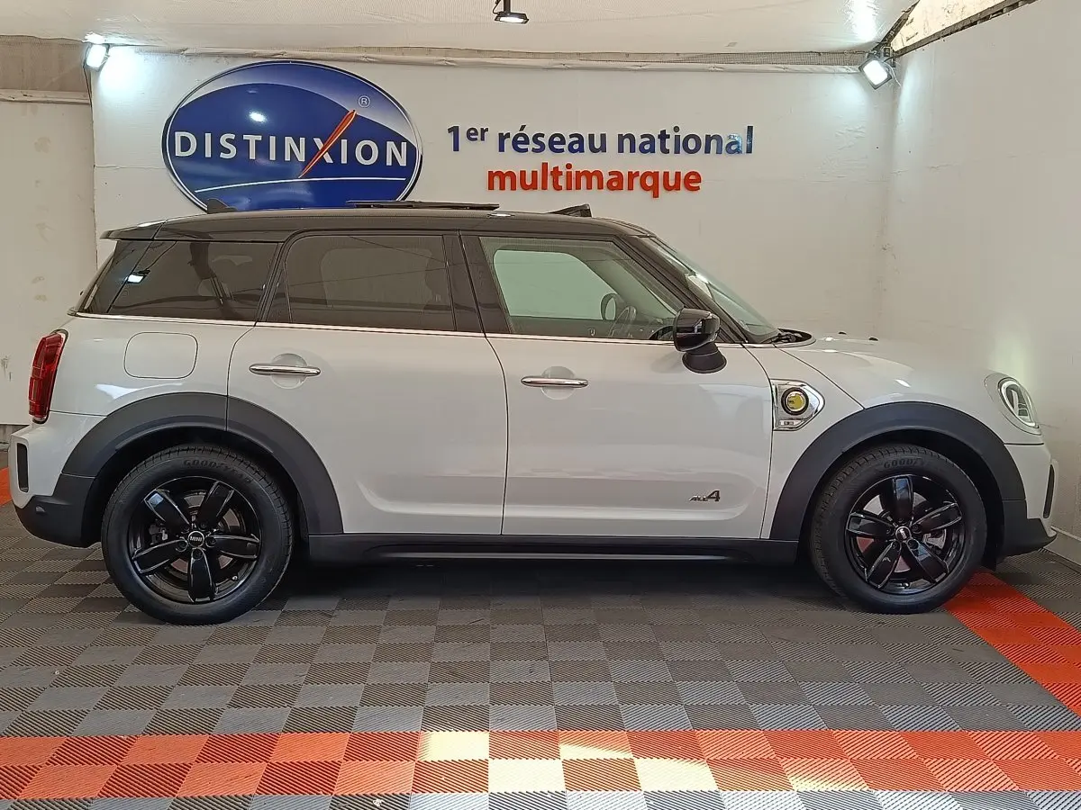 Profil droit d'un MINI COUNTRYMAN Cooper SE blanc avec toit noir et jantes noires dans un showroom.