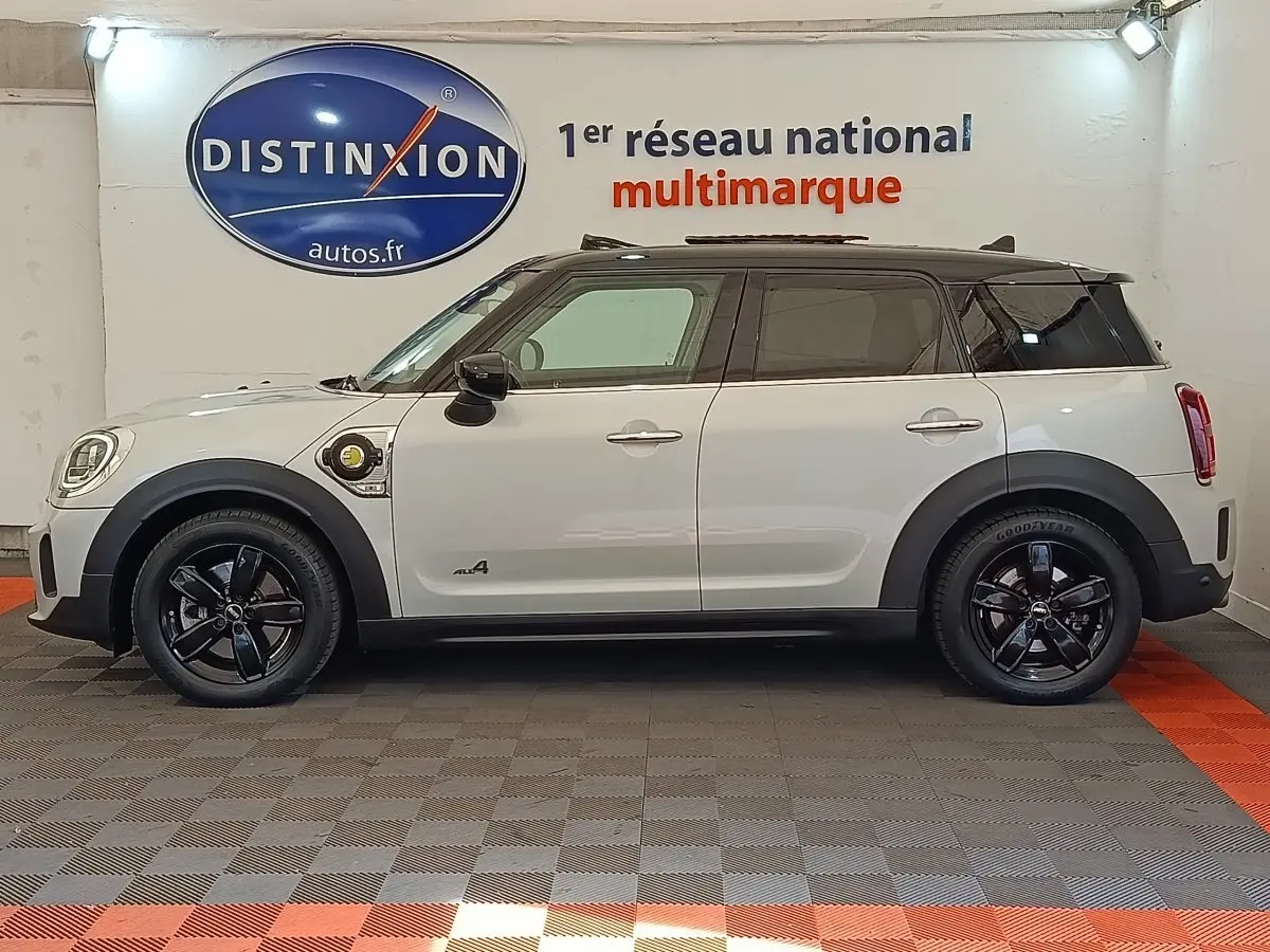 Profil côté gauche d'un MINI Countryman Cooper SE blanc avec jantes noires et prise de recharge visible sur l'aile avant.