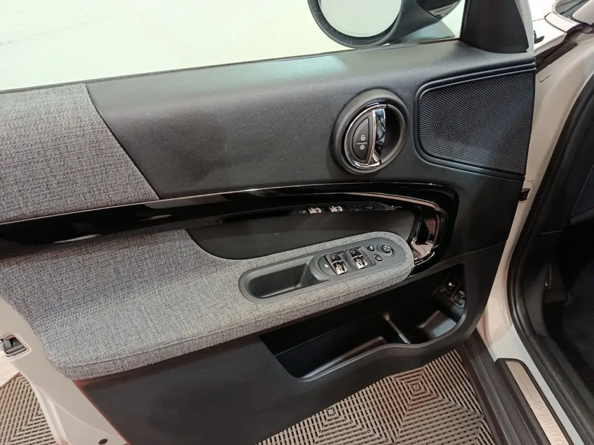 Vue rapprochée de la porte avant gauche blanche du MINI COUNTRYMAN Cooper SE avec garniture tissu gris et commandes électriques.