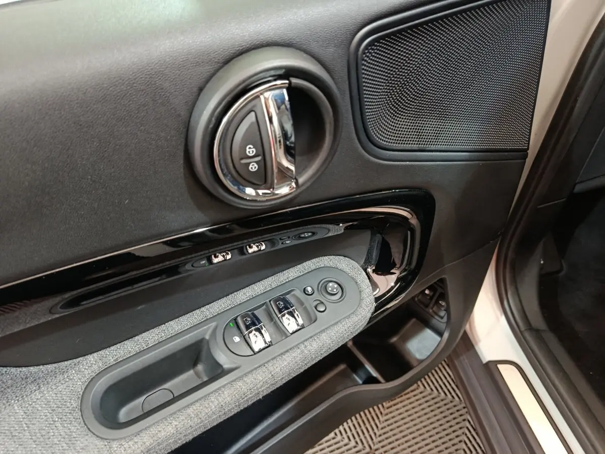 Gros plan sur la portière côté conducteur du MINI Countryman blanc, montrant les commandes de vitres et la poignée chromée.