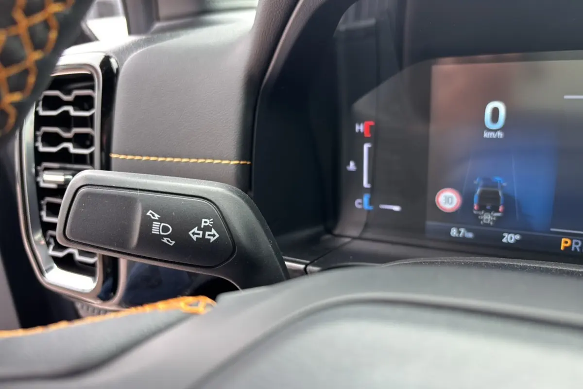 Gros plan sur le commodo gauche et le tableau de bord numérique du Ford Ranger Wildtrak Plus noir agate, avec coutures orange visibles.