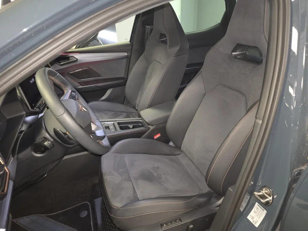 Vue intérieure côté conducteur de la CUPRA Leon 1.5 e-Hybrid 2024 avec sièges baquets suédine noirs et surpiqûres cuivrées.