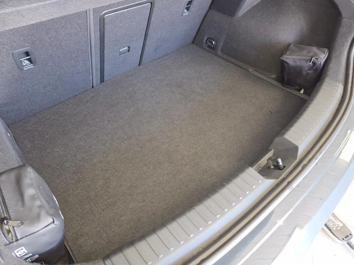 Coffre spacieux vu de dessus de la CUPRA Leon 1.5 e-Hybrid bleu, avec tapis gris et petits rangements latéraux.