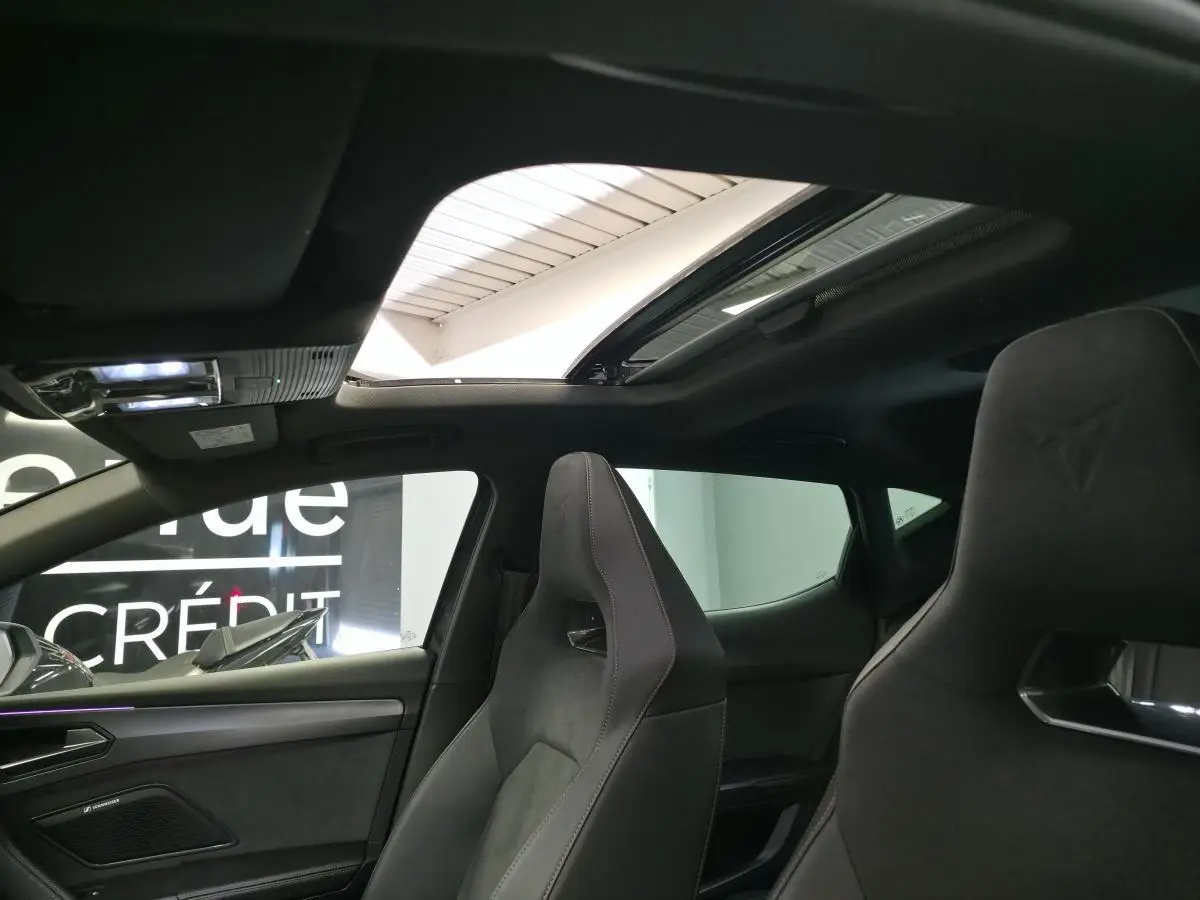 Intérieur de la CUPRA Leon 2024 vu côté droit, sièges baquets noirs avec logo embossé et toit ouvrant panoramique.