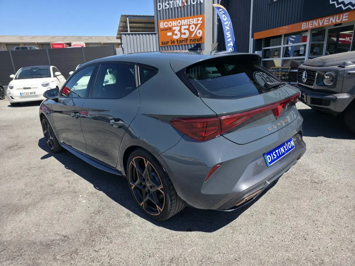 Vue 3/4 arrière droite d'une CUPRA Leon hybride rechargeable bleu Fjord avec jantes alliage 19'' cuivrées et bandeau lumineux arrière.